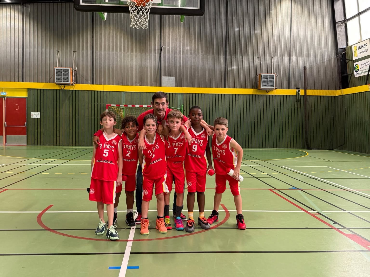 Enfants en maillots rouges et leur encadrant, réunis sur le terrain.