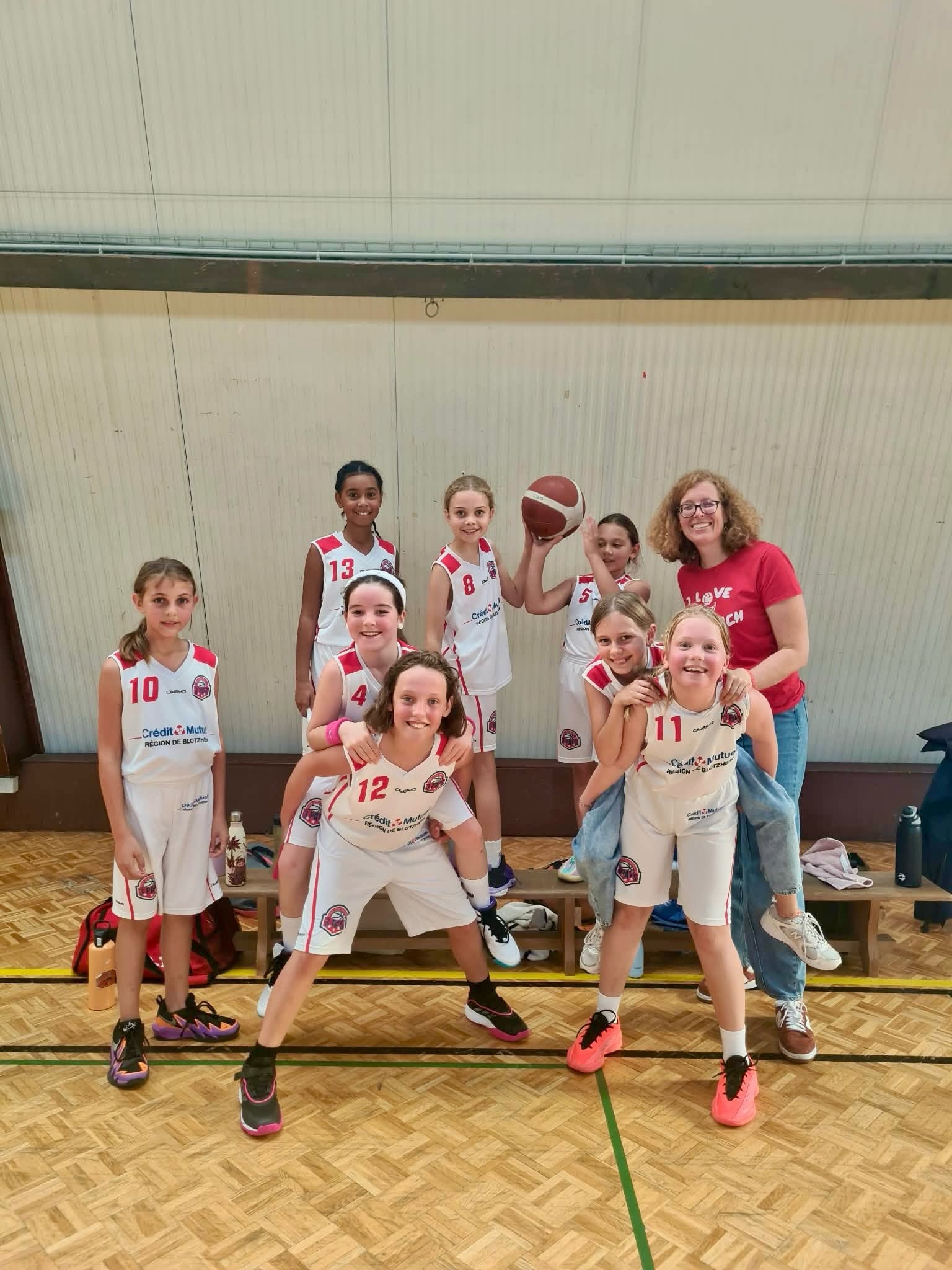 Basketteuses en maillots blancs et rouges, réunies avec leur encadrante.