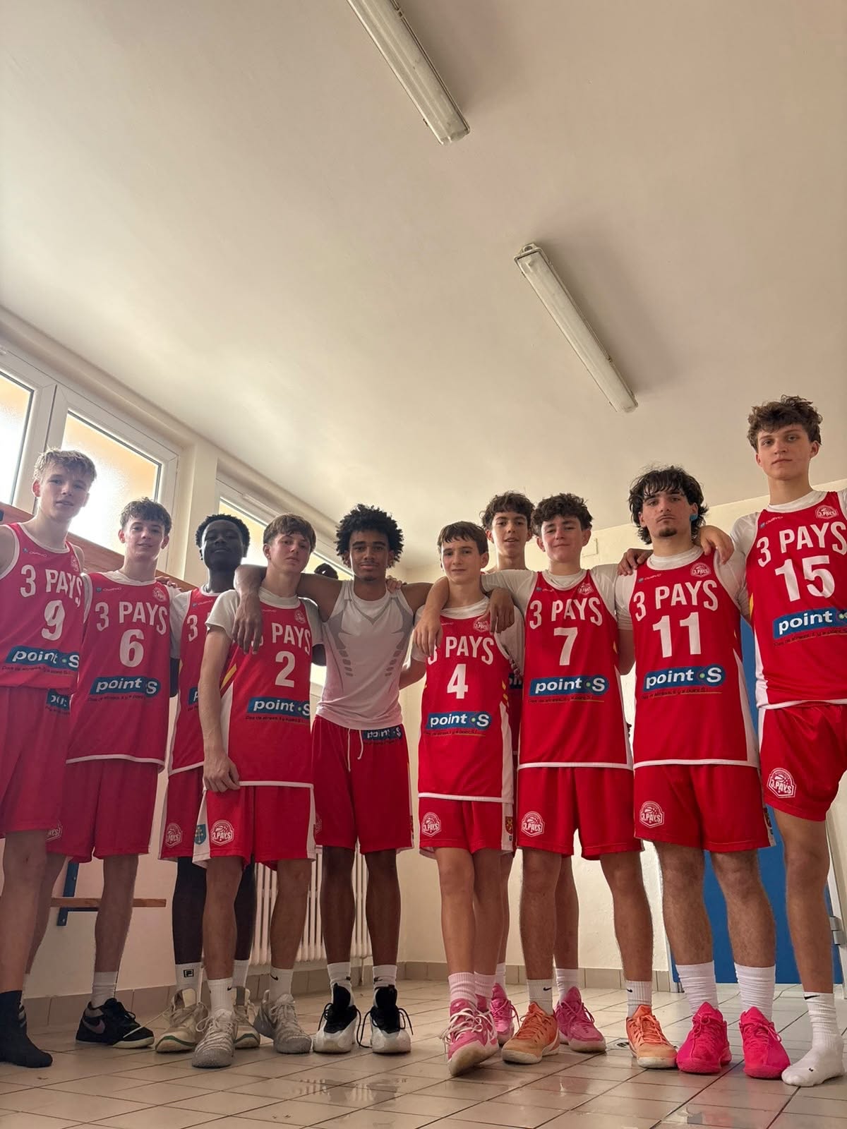 Groupe de basketteurs du club en maillots rouges, réunis dans un vestiaire.