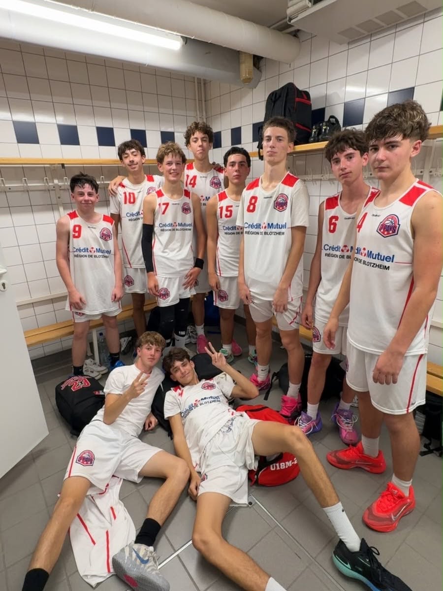 Groupe de basketteurs en maillots blancs et rouges, réunis dans un vestiaire.