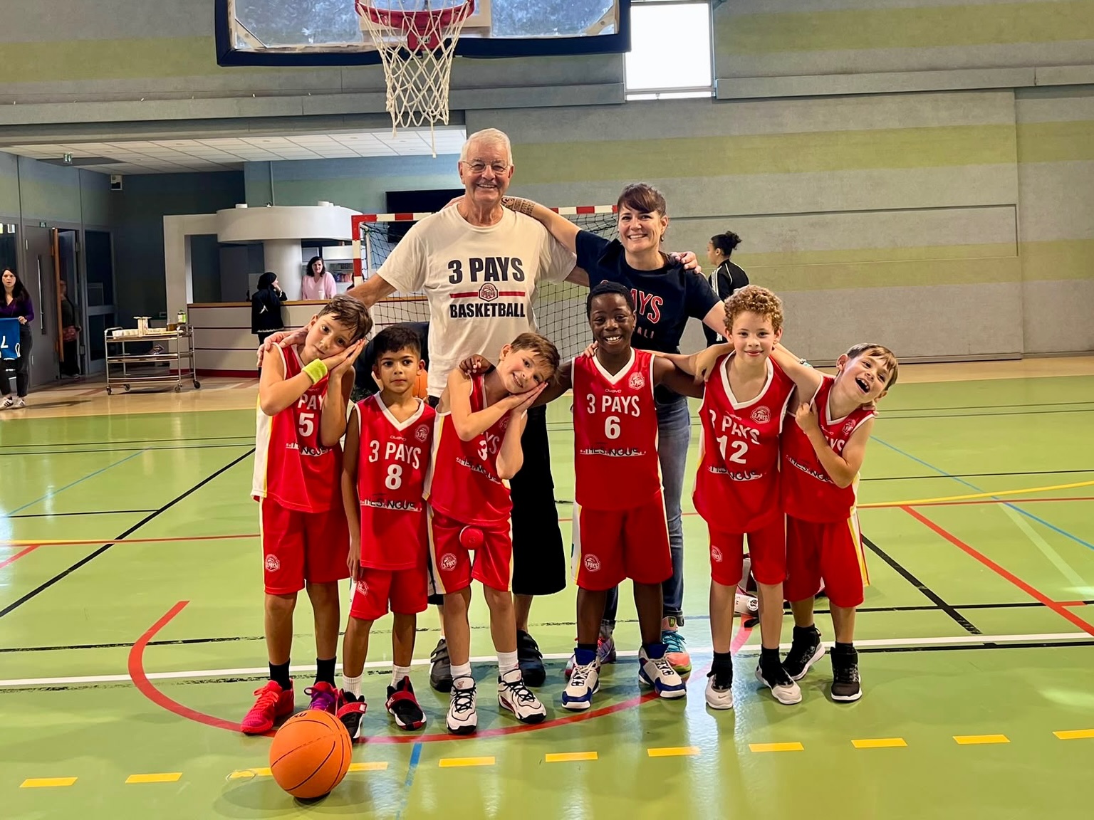 Enfants du club en maillots rouges, réunis avec leurs encadrants sous un panier.