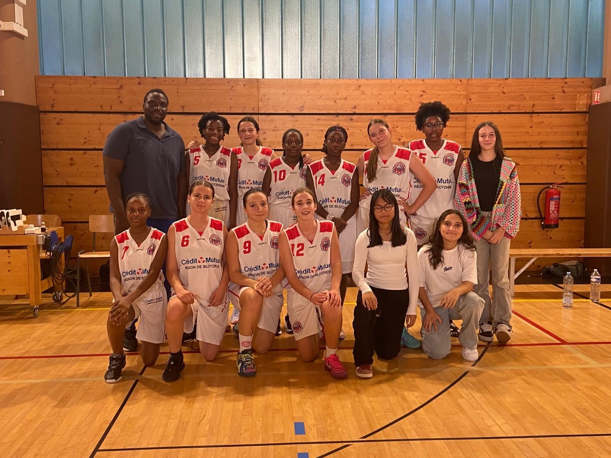 Joueuses en tenue blanche et rouge et leur encadrement, réunis dans une salle de basket.