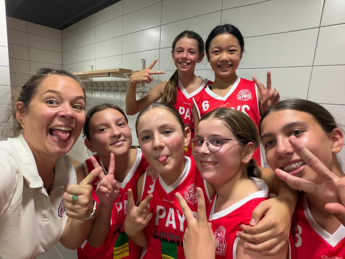 Selfie collectif de jeunes basketteuses en maillots rouges avec leur encadrante.
