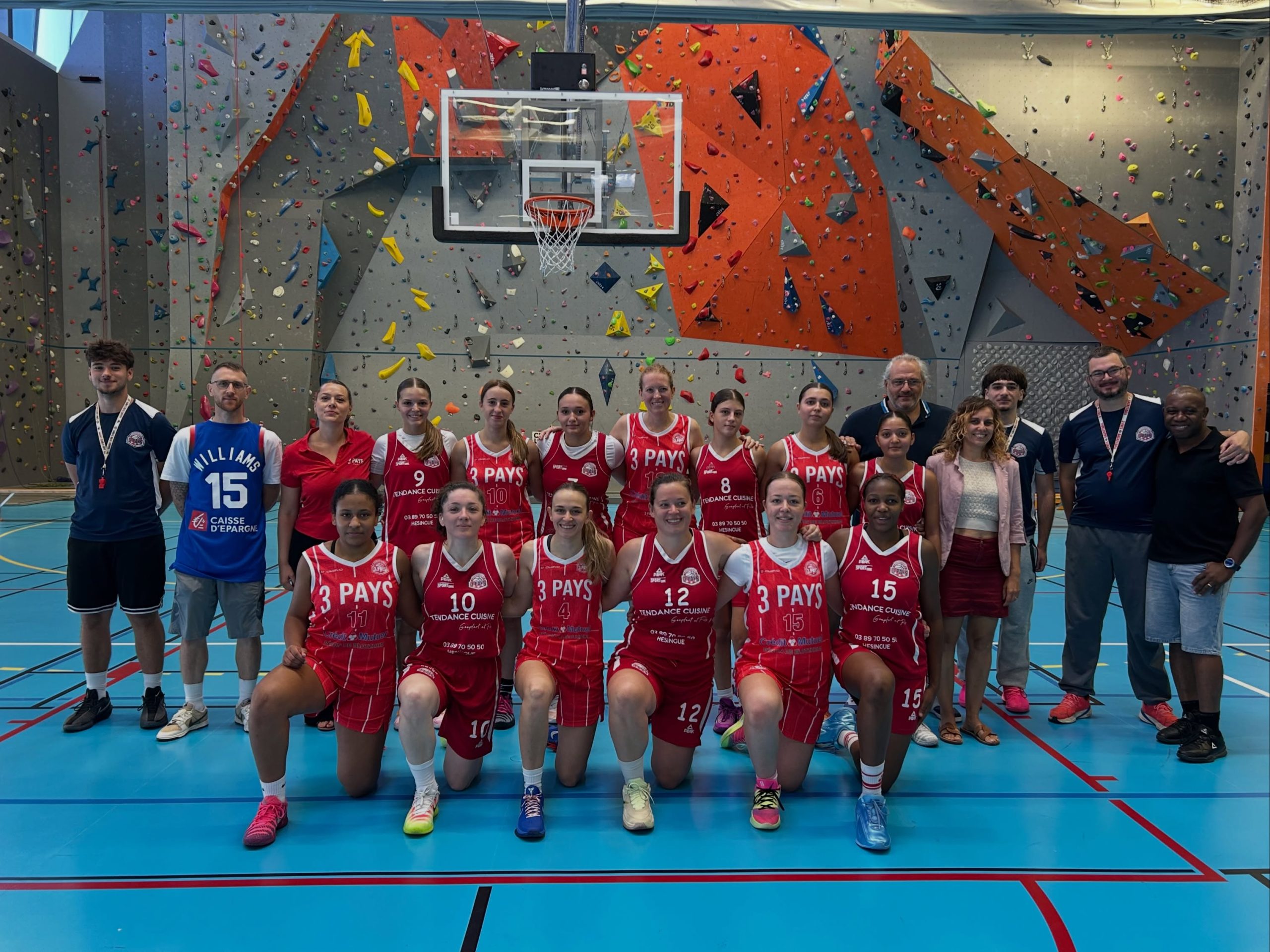 Joueuses et encadrants du club réunis en tenue rouge sur le terrain.