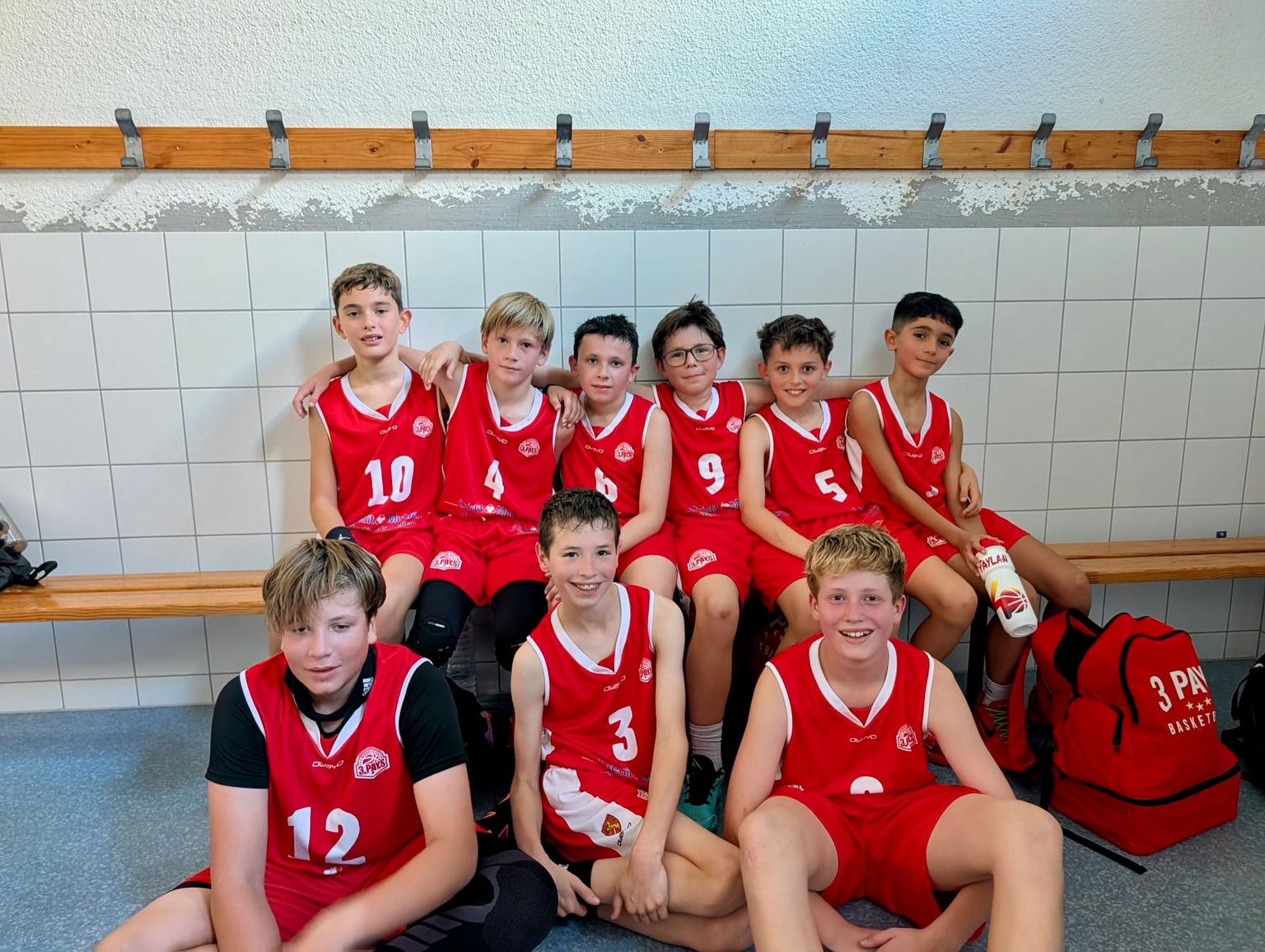 Jeunes en maillots rouges, réunis et souriants dans une salle de basket.