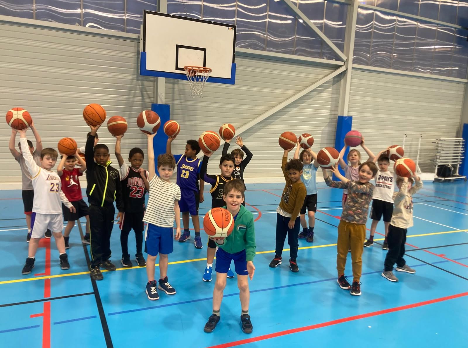 Groupe d’enfants sur le terrain, chacun levant son ballon de basket.